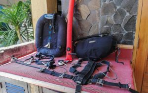 Diving equipment sitting on a bench. A sidemount harness and wing, and backmount wing. Sidemount shorhose and longhose regulators, and a DSMB