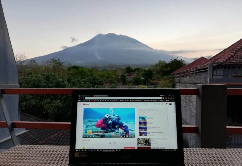 Laptop in the foreground showing IANTD skills on youtube. Mount Agung sits in the background